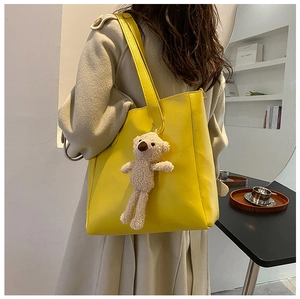 Detail view of a bright yellow matte leather tote bag with a cute plush bear pendant accessory