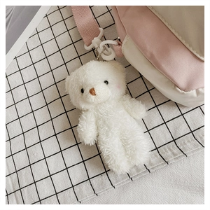 Close-up of white plush bear pendant with curly fur and a plastic hook for bags