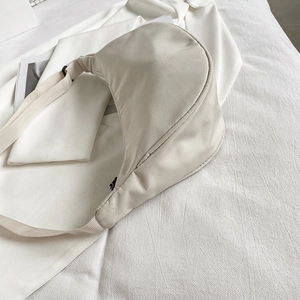 Minimalist cream nylon half-moon crossbody bag with wide strap on a white background