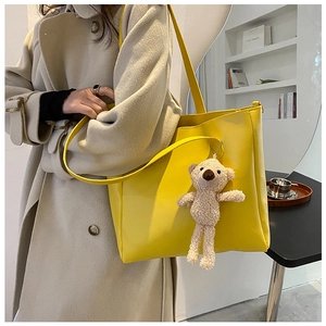 Yellow large capacity PU tote bag with plush bear charm shown on a model in trench coat