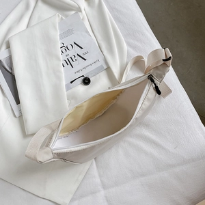 Minimalist white nylon crescent bag with cow print lining and wide strap on white fabric