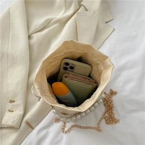 Cream pearl bucket bag with gold chain strap and drawstring closure shown in 45-degree angle