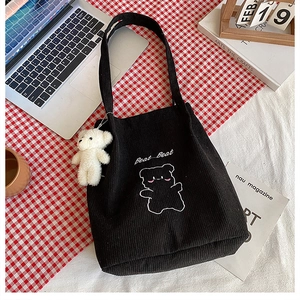 Dettaglio della borsa tote in velluto a coste nera con ricamo di orso e ciondolo peluche