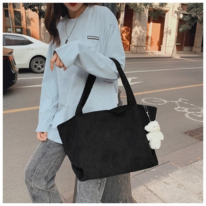 Detail of black corduroy tote bag featuring a cute white plush bear charm in city street