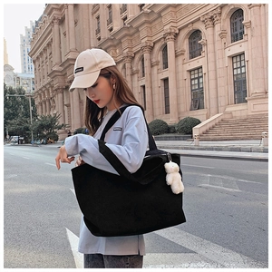 Street style view of a black corduroy tote bag with cute white plush bear keychain