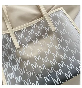 Detail of transparent PVC tote bag with white M-letter print and beige leather handles