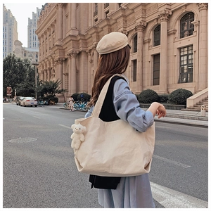 Large cream corduroy tote bag detail with cute plush bear charm on urban background