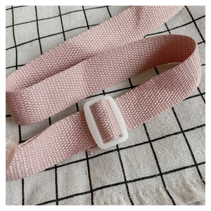 Detail of pink woven shoulder strap with white adjustable plastic buckle on a crossbody bag