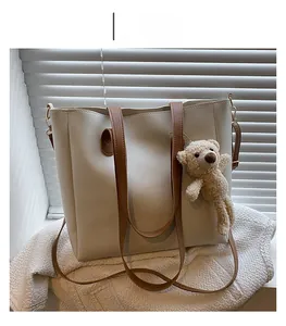 Detail of minimalist cream tote bag with brown straps and cute teddy bear charm