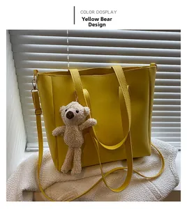 Detail view of yellow faux leather tote bag with a white plush bear charm and straps