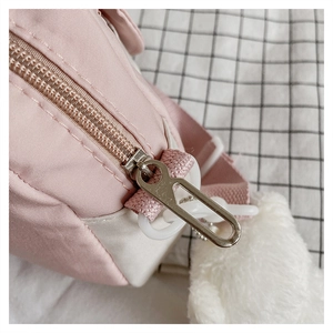 Close-up of pink and white nylon crossbody bag with silver zipper and plush pompom charm