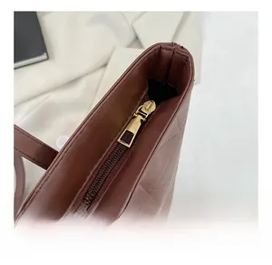 Close-up of smooth gold metal zipper and quilted PU leather texture on brown tote bag