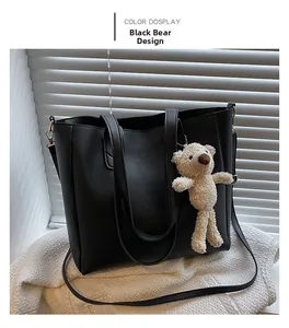 Detail of black faux leather tote bag with a beige plush bear charm and adjustable strap