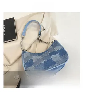 Detail of blue denim baguette bag with silver chain strap on beige blazer background