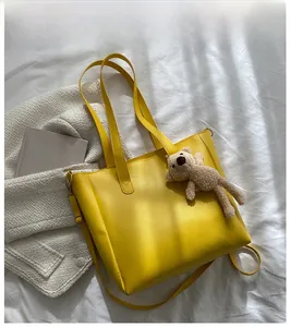 Detail of soft yellow PU leather tote bag with cute brown bear charm on white fabric