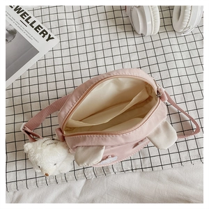 Detail of pink canvas crossbody bag with rabbit ears, plush bear charm, and inner pocket