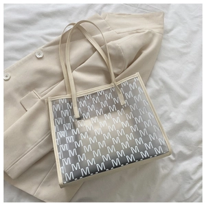 Close-up of a stylish cream PU leather tote bag with M-pattern on a soft blazer