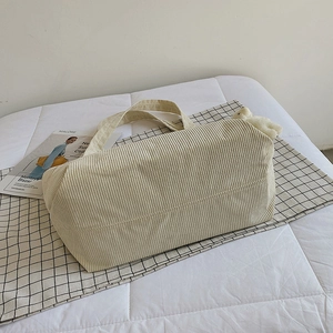 Off-white corduroy tote bag with plush bear charm on minimalist plaid bedding