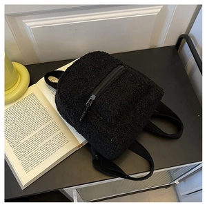 Close-up of black fleece mini backpack on a table with a vintage book and warm lamp