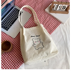 Dettaglio borsa tote in velluto a coste crema con ricamo a forma di orso su sfondo a scacchi