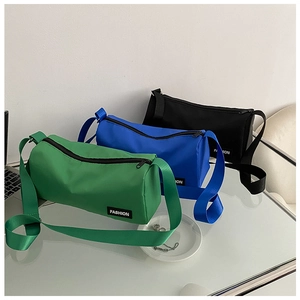 Trois sacs bandoulière cylindriques en nylon vert, bleu et noir posés sur un bureau