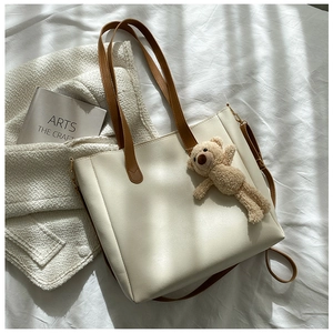 Detail of cream tote bag with dark brown straps and plush bear charm on white fabric