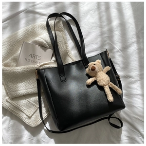 Detail of black faux leather tote bag with top handle and beige teddy bear charm