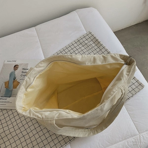 Large corduroy tote bag in beige with yellow lining and top zip closure on white bedding