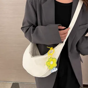 Détail d'un sac demi-lune en toile crème avec un charmant pendentif en fleur jaune vif