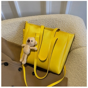 Yellow faux leather tote bag on a beige sofa with a cute brown teddy bear keychain