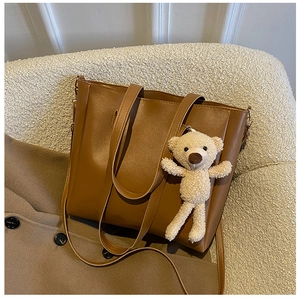 Brown leather tote bag with a cute plush bear pendant and long shoulder strap detail