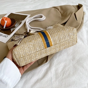 Large woven straw tote bag with blue stripes and white rope handles in a casual setting