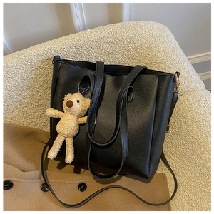 Detail of a black leather tote bag with a cute plush bear pendant on a cozy chair