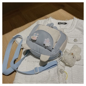 Detail of cute blue and beige canvas crossbody bag with fluffy bear pendant and bunny patch