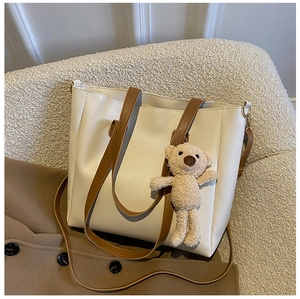 Detail of a beige tote bag on a knit sofa with plush bear charm and brown strap
