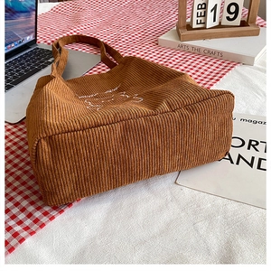 Primo piano della borsa tote in velluto a coste marrone con ricami bianchi e texture