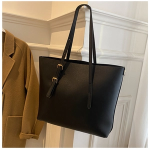 Close-up of black matte leather tote bag with gold buckle detail beside a wool coat
