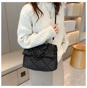 Detail view of a black quilted chain crossbody bag styled with a white cable knit sweater