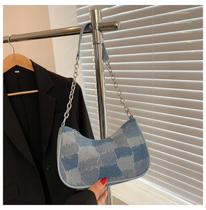 Detail of blue denim patchwork baguette bag with silver chain strap on metal hanger