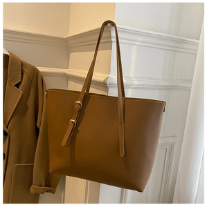 Detail of tan faux leather tote bag with adjustable strap and metal buckle on white wall