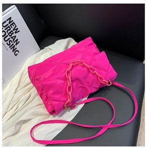 Detail of bright pink quilted crossbody bag with chunky chain handle on a black background