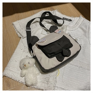 Close-up of a cartoon bear-ear crossbody bag with a white plush bear pendant on a tweed top