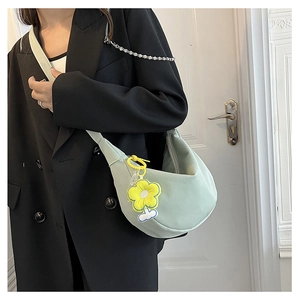 Détail du sac croissant vert clair avec charm fleur jaune porté par un modèle
