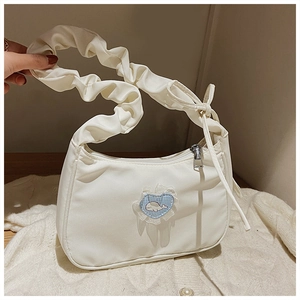Detail einer weißen Faltenhandtasche mit Herz-Spitzen-Patch und Wal-Motiv auf beigem Grund
