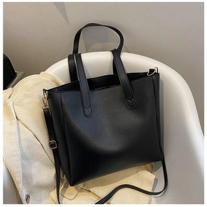 Detail of minimalist black faux leather tote bag with gold hardware on a chair