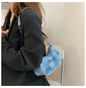 Detail of light blue patchwork denim baguette bag with metal chain strap worn by model