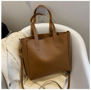 Detail of a brown faux leather tote bag with top handles on a modern white chair