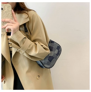 Detail of vintage patchwork denim baguette bag with leather strap on a beige coat