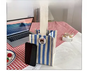Size comparison of a blue and white striped canvas handbag next to a smartphone