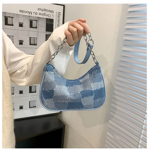 Close-up of crescent denim baguette bag with silver chain strap and patch details